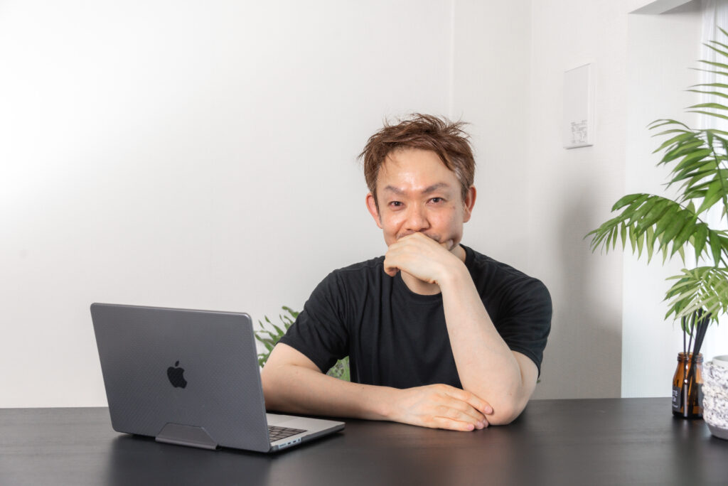 口元に手を当てて考えるタク(井上琢磨)